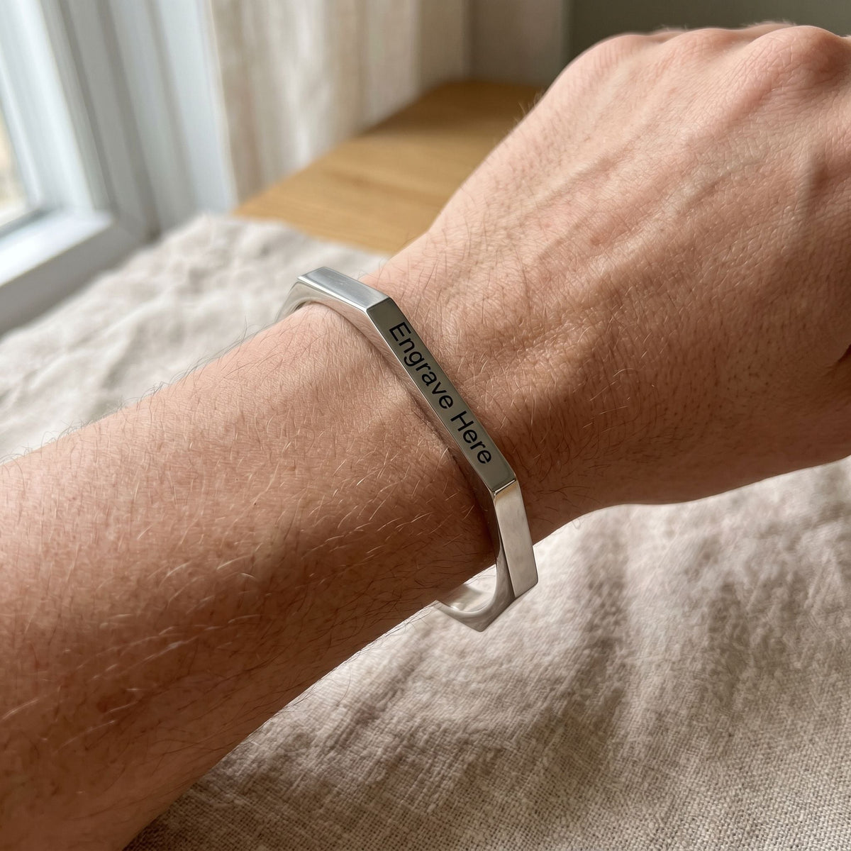 Close-up of model's wrist showcasing designer engraved hexagon karha bracelet in natural lighting with subtle surface highlights.