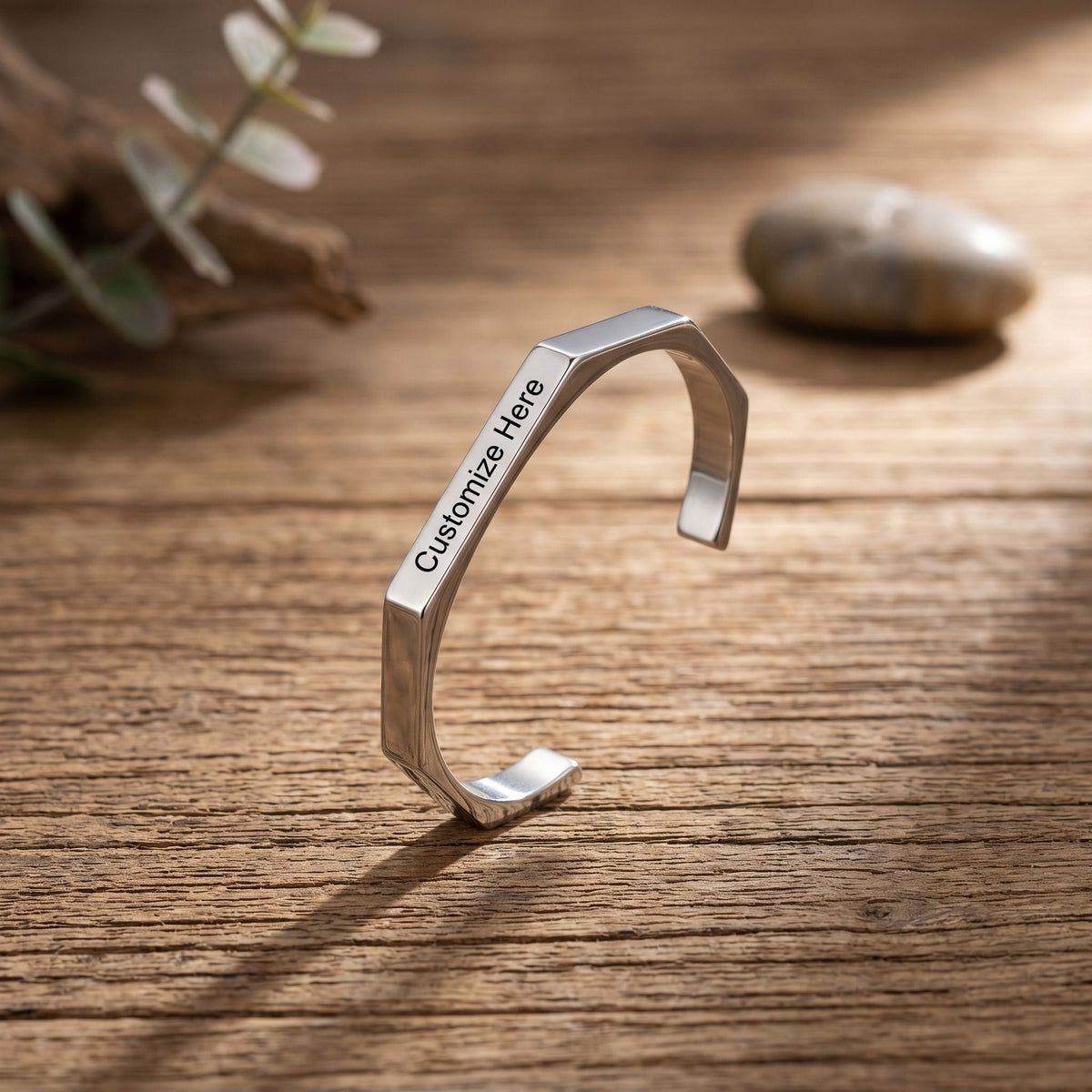 Side view of tiny engraved hexagon karha bracelet on textured wood emphasizing slim profile and reflective finish.